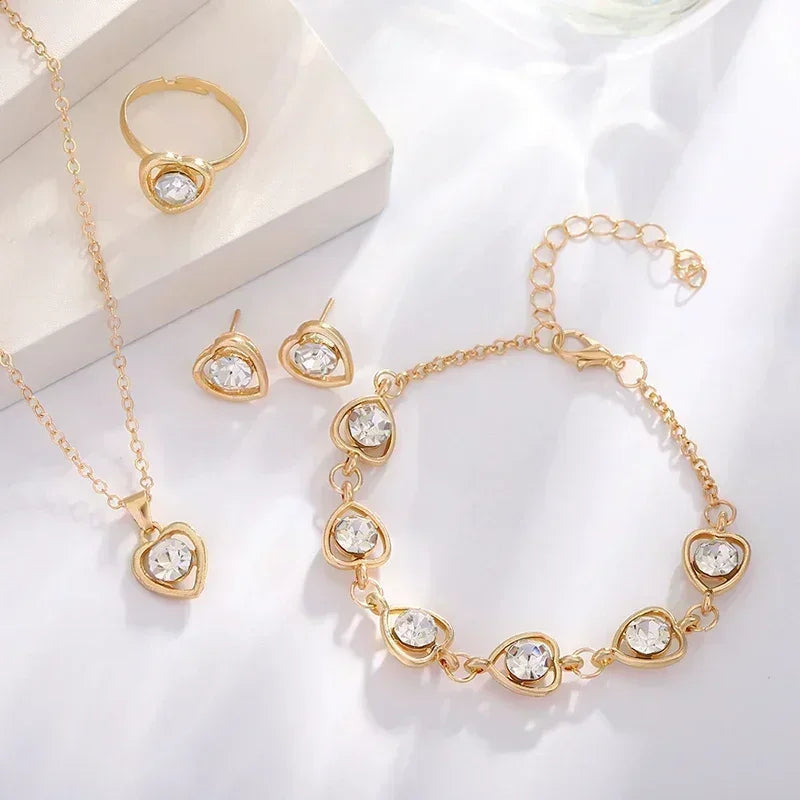 Gold jewelry set with heart-shaped clear crystals includes ring, earrings, necklace, and bracelet displayed on white background
