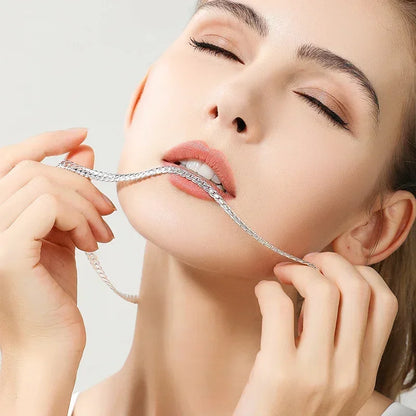 Close-up of woman with closed eyes biting silver chain necklace, showcasing elegant jewelry