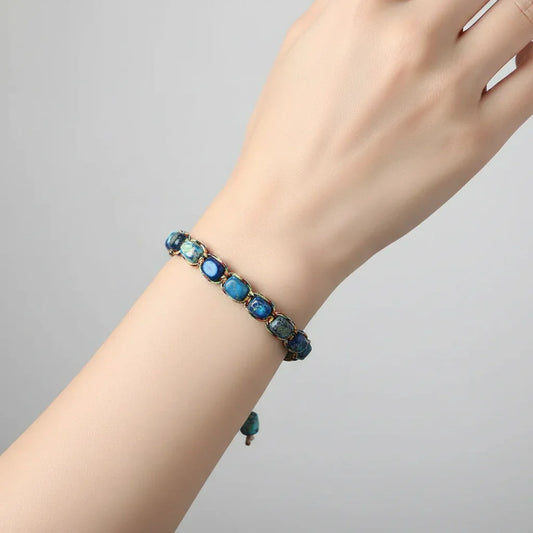 Close-up of a wrist wearing a blue stone beaded bracelet against a plain light gray background