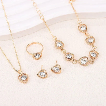 Gold jewelry set with heart-shaped clear crystals including necklace, bracelet, ring, and earrings on white background