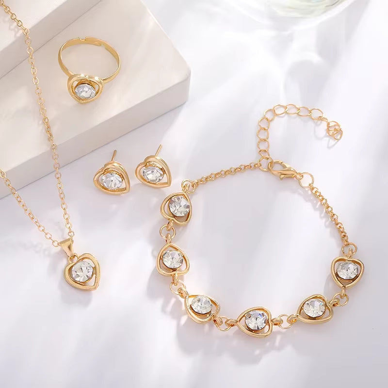 Gold jewelry set with heart-shaped clear crystals including necklace, ring, earrings, and bracelet on white background