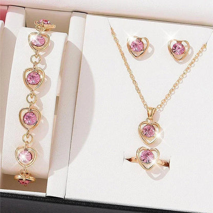 Gold heart-shaped jewelry set with pink gemstones including bracelet, necklace, earrings, and ring on white display